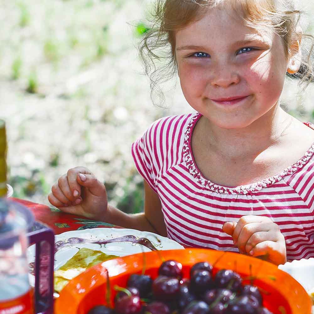 Ett barn äter mat från en barntallrik på sommaren vid ett bord utomhus.